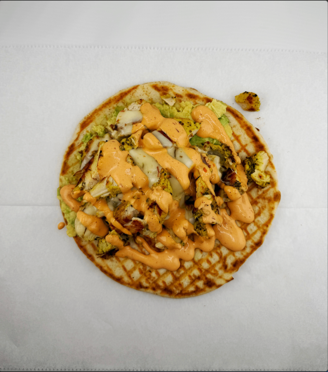 Grilled chicken flatbread topped with avocado, melted cheese, and orange sauce