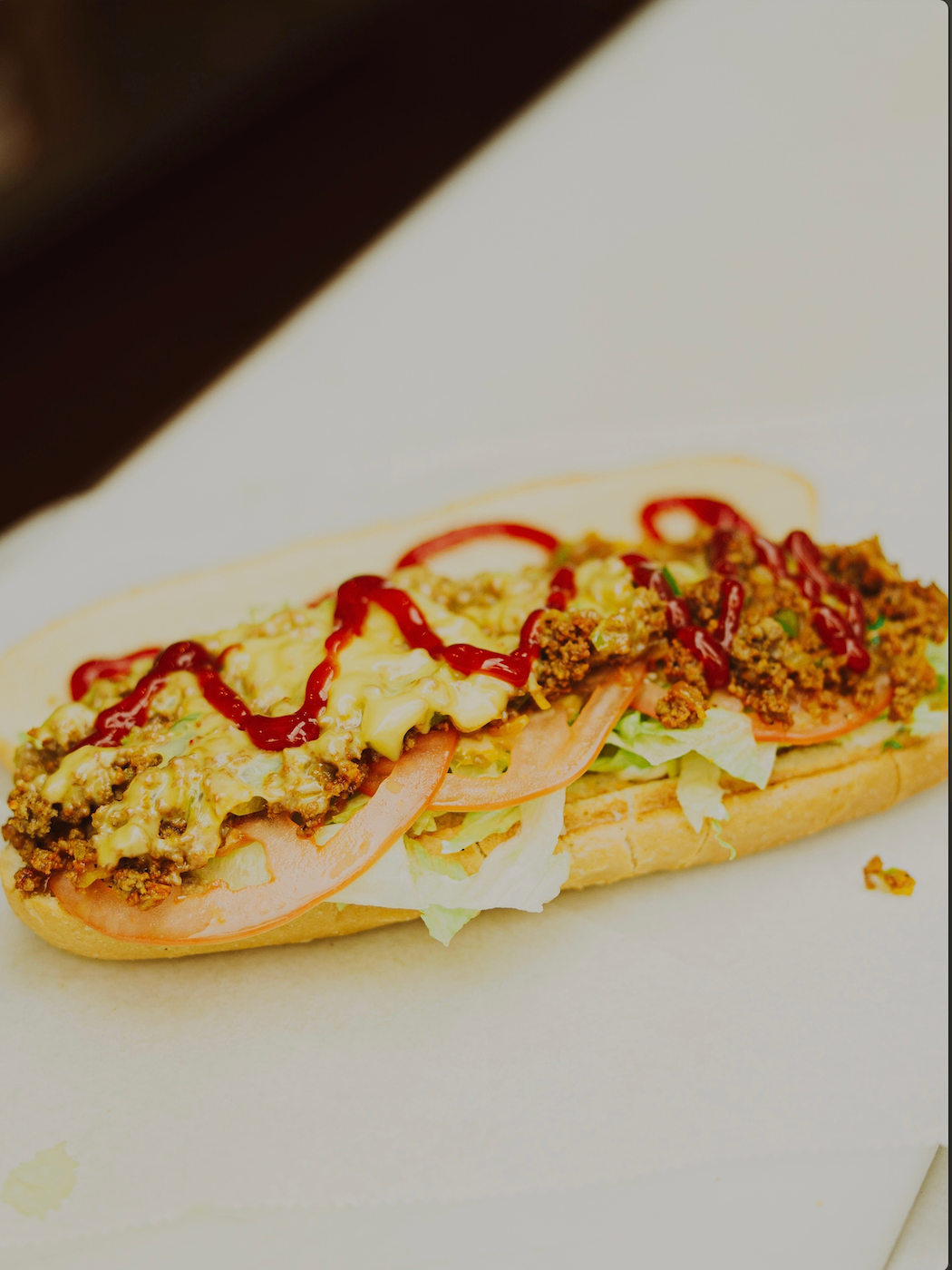 Classic cheesesteak sub with melted cheese, tomato, lettuce, and ketchup drizzle