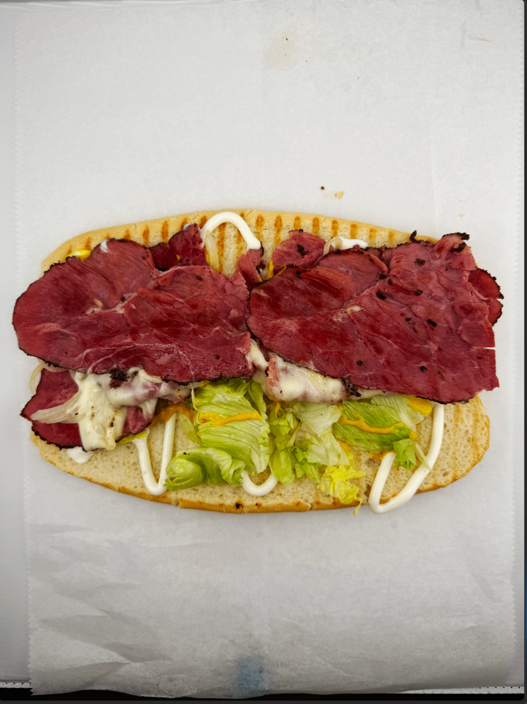 Hot pastrami melt layered with cheese, lettuce, mustard, and mayo on a pressed roll