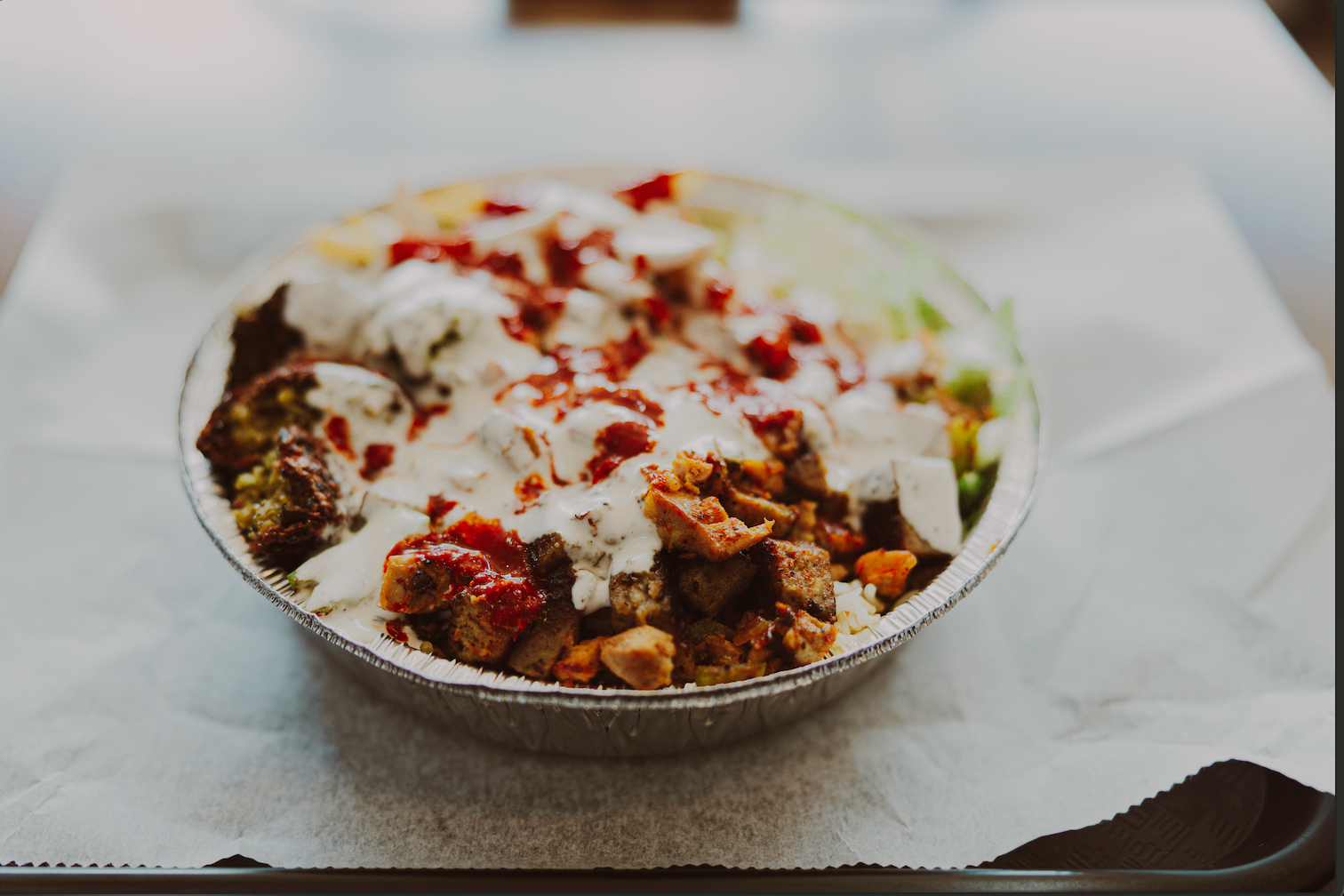 Mixed protein bowl with rice, salad, white sauce, and red sauce